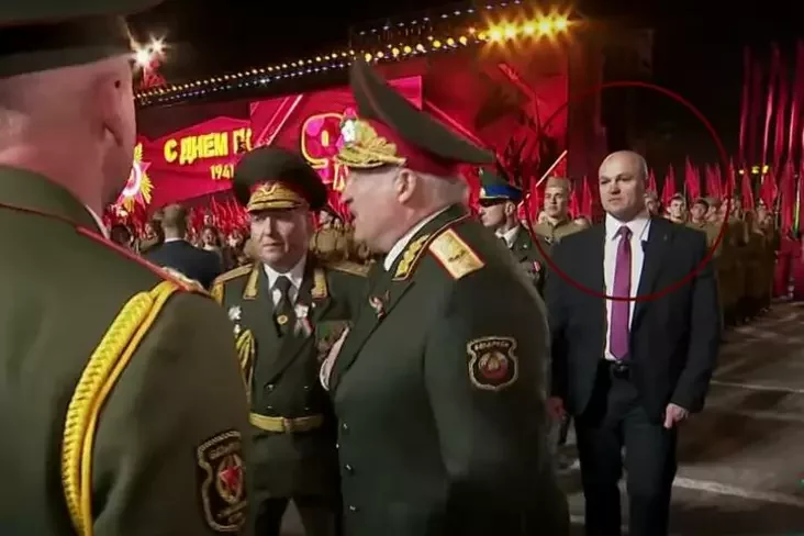 Pavieł Łahun stoit za śpinoj Aleksandra Łukašienko. Minsk, 9 maja 2025 hoda. Kadr vidieo YouTube-kanała news.by